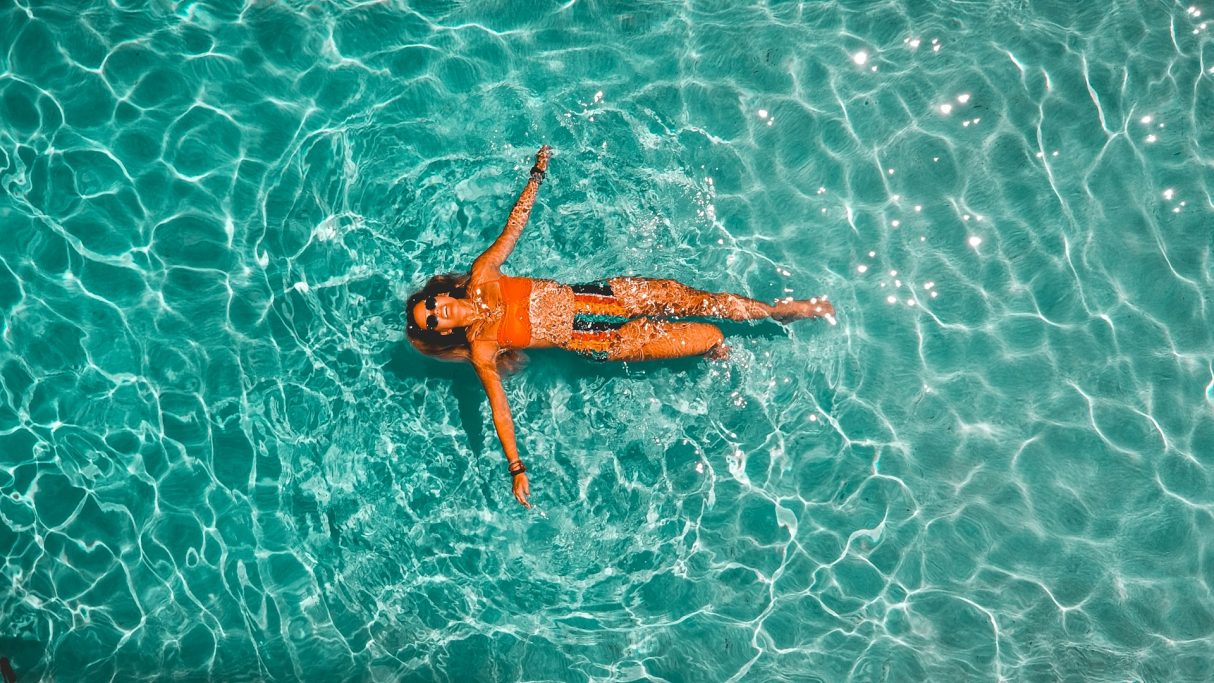 Mujer flotando en una piscina de agua clara y brillante.