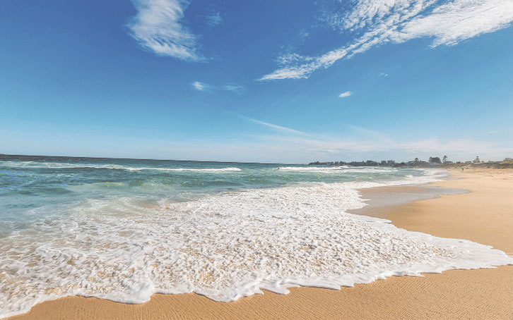 Playa de arena con olas suaves y cielo despejado.