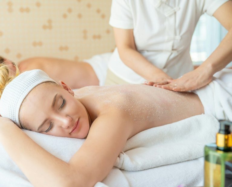 Mujer recibiendo un masaje relajante en un spa, con otra persona en el fondo.