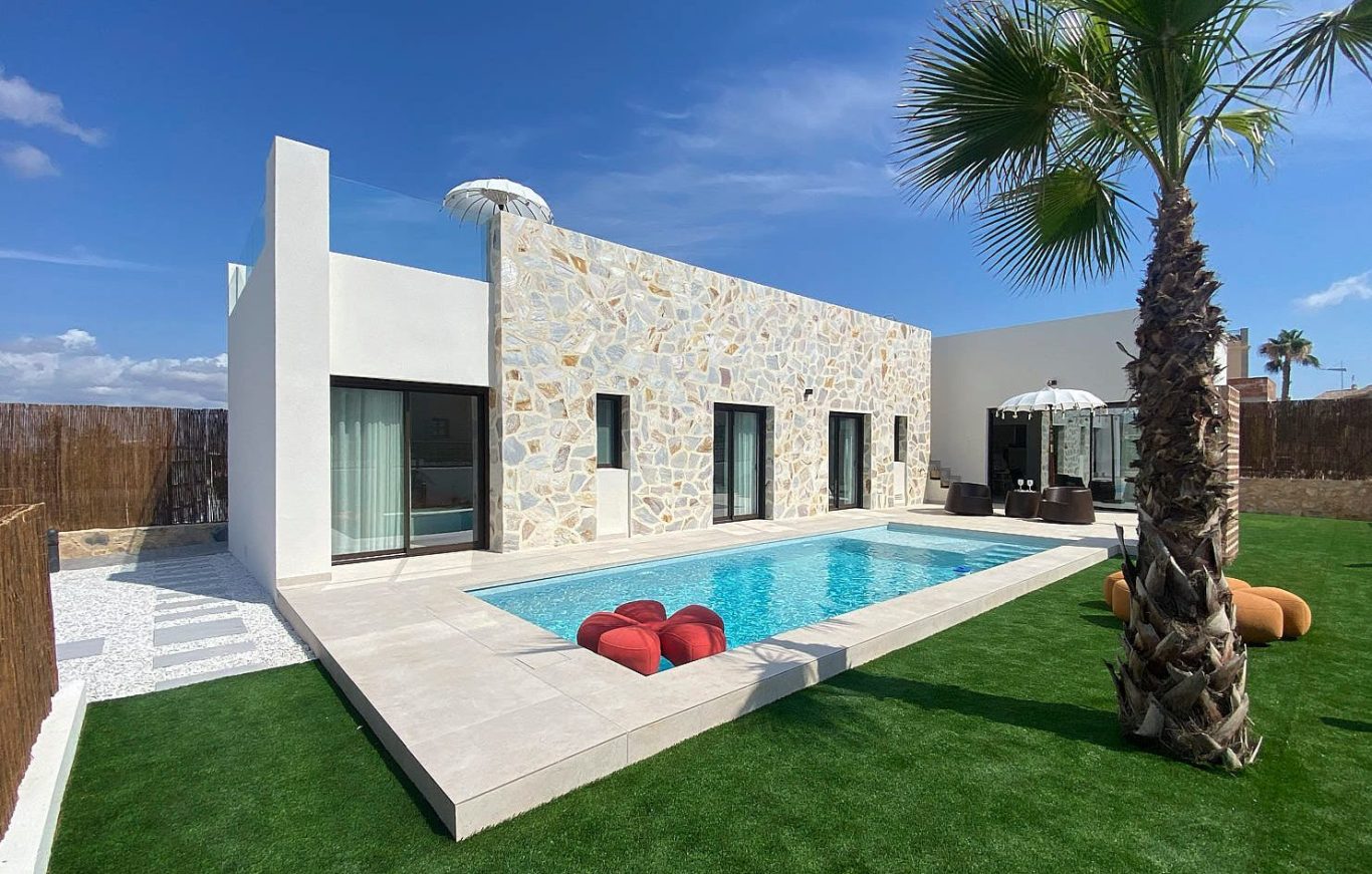 Casa moderna con piscina, jardín y palmera, decorada con muebles exteriores.